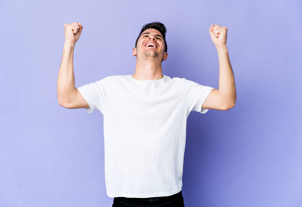 Young caucasian man isolated on purple background raising fist after a victory, winner concept. - Foto, Bild