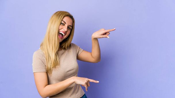 Молода блондинка ізольована на фіолетовому фоні, збуджена, вказуючи з палець
. - Фото, зображення