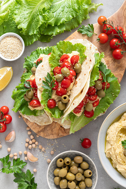 Tortilla wraps with chickpea hummus, fresh tomatoes and olives, vegan food - 写真・画像