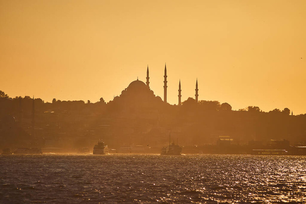 シティラインフェリーやボートでイスタンブールシルエットの上の日没。日没のミナレットのシルエットを持つ伝統的なアラビアの町、トルコのイスラム建築の古代のランドマーク. - 写真・画像
