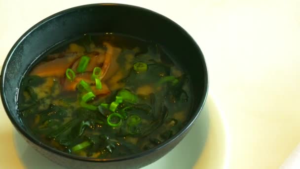 Miso soup in the big black bowl. It is traditional japanese food. Main ingredients are miso paste, tofu, wakame seaweed and shiitake mushrooms. 4K - Footage, Video