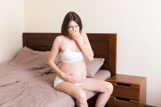 Вагітна страждає від нудоти. Симптоми вагітності, очікування токсикозу. Молода блювання жінка сидить у ліжку. концепція батьківства
. - Фото, зображення