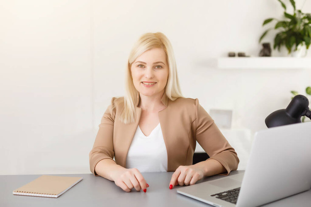 Portrait of happy skilled middle aged woman life coach, business consultant, psychologist or medical advisor smiling joyfully at camera, working on laptop, enjoying her job, helping people online - Fotó, kép