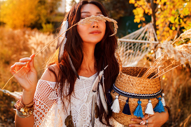 Portrait of a beautiful boho woman in a sunny field at sunset. - Photo, Image