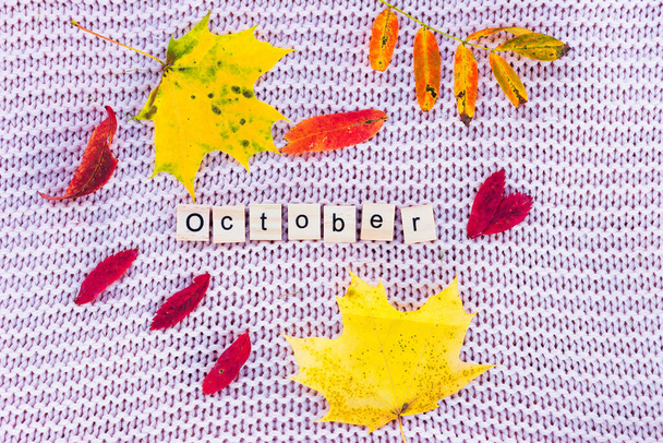 A yellow sheet and the words october lie on a knitted background. - Photo, image