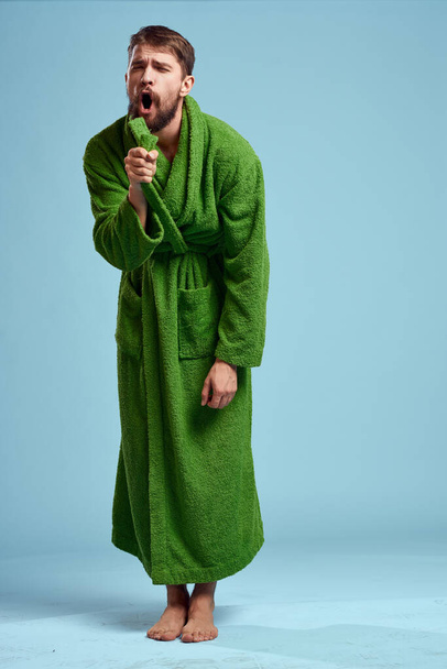 a man in a green robe in full growth on a blue background barefoot - Photo, Image
