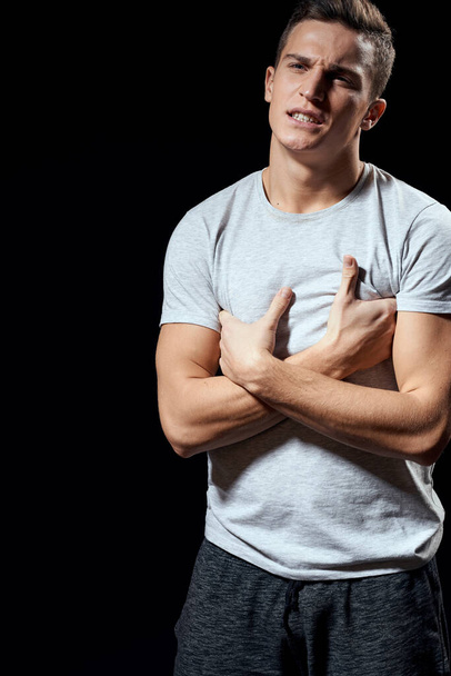 красивый мужчина в белой футболке на черном фоне надутые мышцы рук спортивная модель обрезанный вид - Фото, изображение