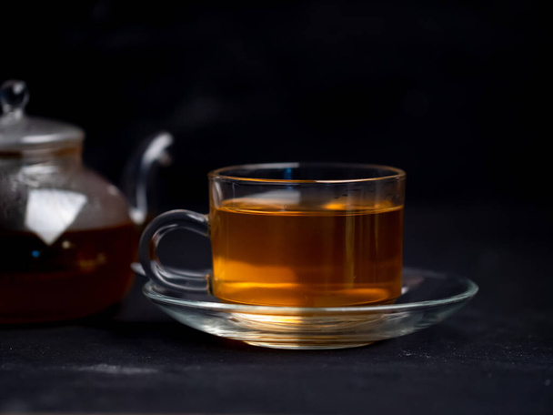 A cup of freshly brewed hot tea and a teapot on the table with a black backgrounds. - Foto, afbeelding