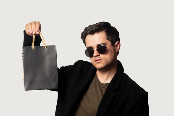 Στυλ τύπος σε μαύρο παλτό και γυαλιά ηλίου με μικρή τσάντα ψώνια - Φωτογραφία, εικόνα