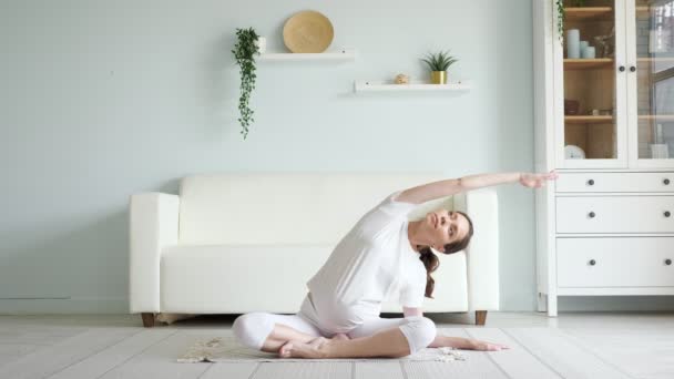 Brunette pregnant woman does side bends on floor at home - Felvétel, videó