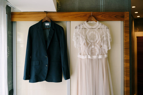 El vestido de novia y la chaqueta de novio en perchas de madera, cuelgan en el armario. - Foto, Imagen