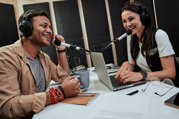 Портатив двух счастливых радиоведущих, молодых мужчин и женщин, разговаривающих друг с другом во время выступления в студии - Фото, изображение