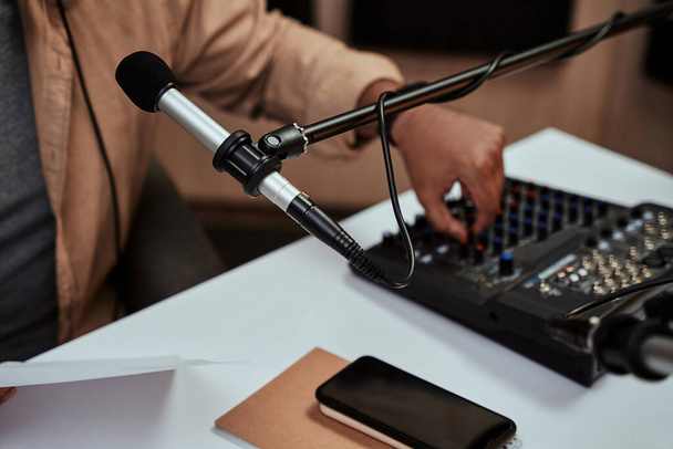 Feche o microfone no estúdio da estação de rádio. host masculino trabalhando em uma mesa de mistura de som em estúdio, ajustando níveis, aumentando o volume em segundo plano - Foto, Imagem