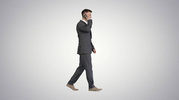 Бізнесмен ходить і розмовляє на мобільному телефоні на градієнті назад
 - Фото, зображення