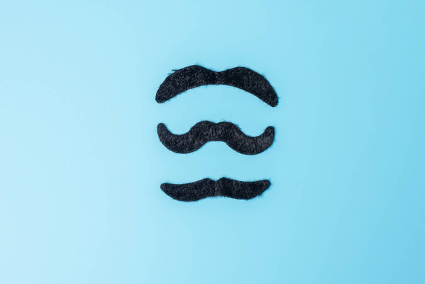 Schwarzer Schnurrbart auf blauem Hintergrund. Happy Vatertag und Internationaler Männertag - Foto, Bild