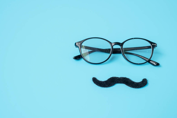 青を基調としたミニマルな黒の口ひげと眼鏡。幸せな父の日と国際男性の日の概念 - 写真・画像