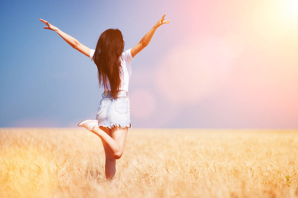 Happy woman enjoying the life in the field Nature beauty, blue sky and field with golden wheat. Outdoor lifestyle. Freedom concept. Woman jump in summer field - Foto, Imagem