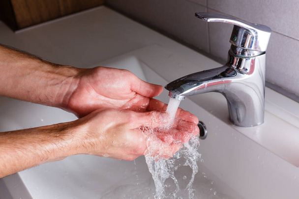 man washes his hands near the white washbasin - Photo, image
