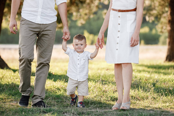 View on toddler. Mother, father hold hands son walk in the park. Young family spending time together on vacation, outdoors. The concept of family summer holiday. selective focus. - Фото, изображение