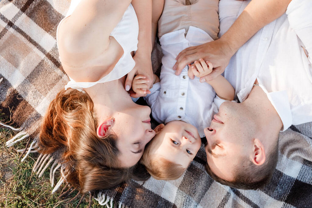 Mom, dad and little son lying on the blanket in the summer park. The concept of summer holiday. Mother's, father's, baby's day. Family spending time together on nature. Family look. - Foto, imagen