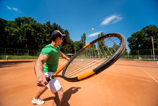 Young athletic man playing tennis on the court. - Foto, afbeelding