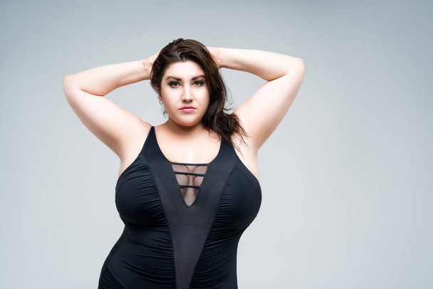 Sexy plus size fashion model in black one-piece swimsuit, fat woman in lingerie on gray background, body positive concept - Фото, изображение