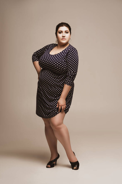 Plus size fashion model in polka dot dress, fat woman on studio background, body positive concept - Foto, afbeelding