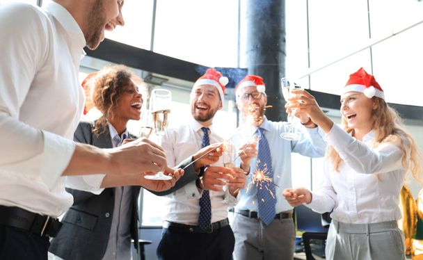 Young business partners are lighting bengal lights and drinking champagne in a modern office. Merry Christmas and Happy New Year - Foto, imagen