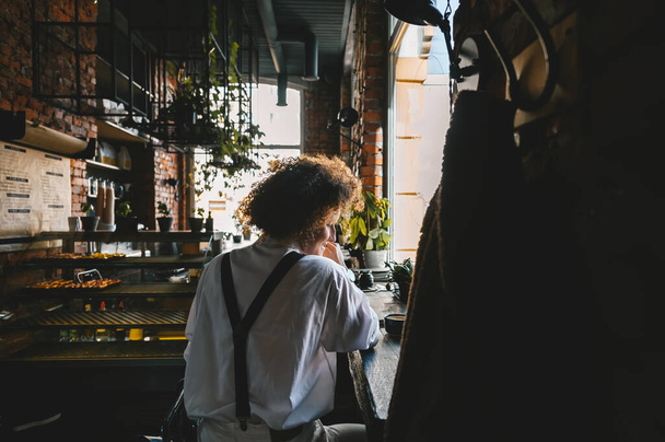 View back of woman with afro hairstyle, who is sitting in the coffee shop or co-working space and looking at mobile phone. - Photo, image