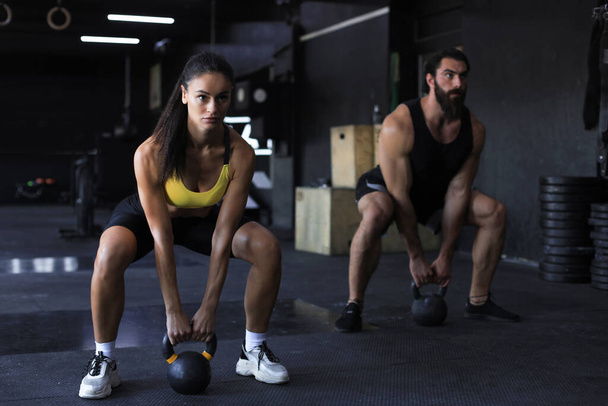 Fit and muscular couple focused on lifting a dumbbell during an exercise class in a gym - Photo, image