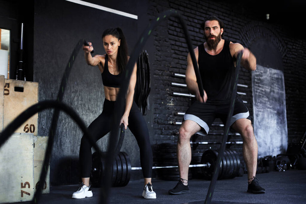 Athletic young indian couple with battle rope doing exercise in functional training fitness gym - Φωτογραφία, εικόνα