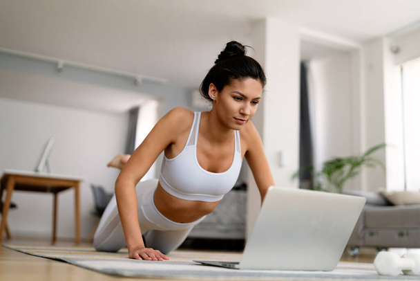 Nuori sovi nainen urheiluvaatteet katsella online video kunto harjoituksia kannettavan tietokoneen kotona - Valokuva, kuva
