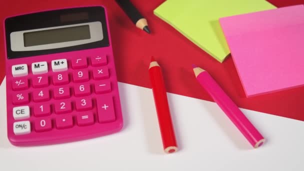 biały papier i kalkulator oraz kredki na czerwonym biurku - Materiał filmowy, wideo