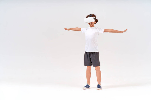 VR technology. Full-length shot of teenage boy in sport clothes wearing virtual reality or 3d glasses exercising isolated over grey background - Foto, immagini