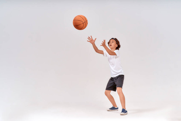 Gól. Teljes hosszúságú felvétel egy tinédzser fiúról, aki kosárlabdázik, miközben elszigetelve áll szürke háttér felett, stúdiófelvétel. - Fotó, kép