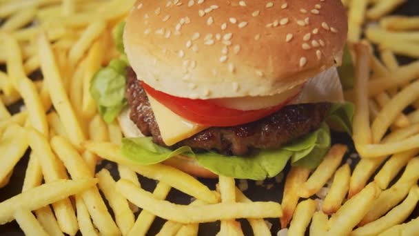 νόστιμο cheeseburger περιβάλλεται από τηγανητές πατάτες σε ένα μαύρο τραπέζι - Πλάνα, βίντεο