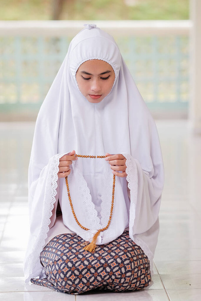 Προσευχή γυναίκα με παραδοσιακές ισλαμικές χάντρες στο χέρι και γονατίζει σε ένα τζαμί. - Φωτογραφία, εικόνα