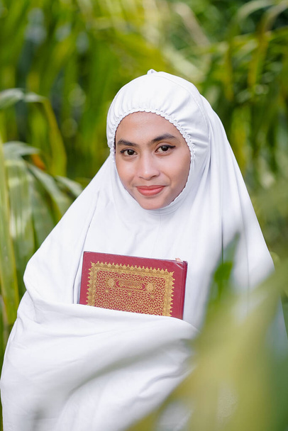Beautiful Muslim women  hand holding Quran   in a green tree garden, Muslim education concept - Photo, Image