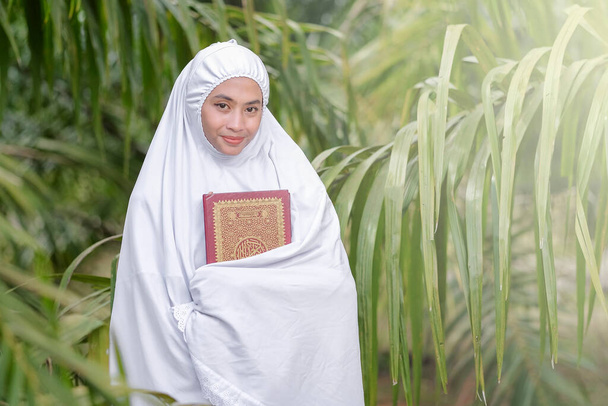Schöne muslimische Frauen halten den Koran in einem grünen Baumgarten in der Hand, muslimisches Bildungskonzept - Foto, Bild