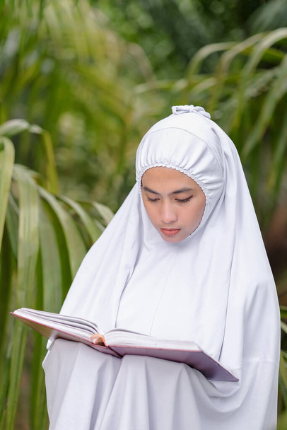 Gyönyörű muszlim nők kéz gazdaság Korán egy zöld fa kert, muszlim oktatási koncepció - Fotó, kép