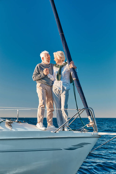 Vakantie. Volledige lengte van gelukkig senior paar in de liefde hand in hand en kijken naar elkaar terwijl ze op de zijkant van zeilboot of jacht dek drijven in zee - Foto, afbeelding