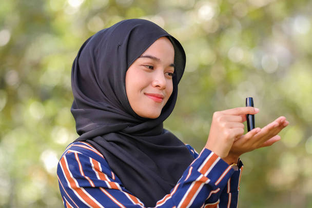 Mosolygós gyönyörű fiatal muszlim nő visel hidzsáb és a kezében egy rúzs homályos háttér. - Fotó, kép