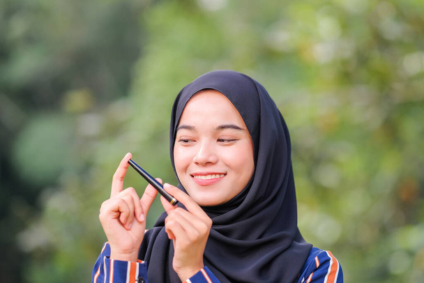 Mooie hijab meisje dragen moderne jurk houden mascara fles over groene achtergrond. Schoonheidsproduct scheut concept. - Foto, afbeelding