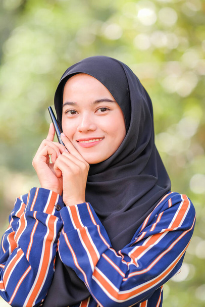 Beautiful hijab girl wearing modern dress holding mascara bottle over green background. Beauty product shoot concept. - Photo, Image