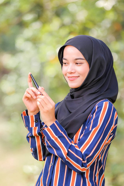 Beautiful hijab girl wearing modern dress holding mascara bottle over green background. Beauty product shoot concept. - Photo, Image