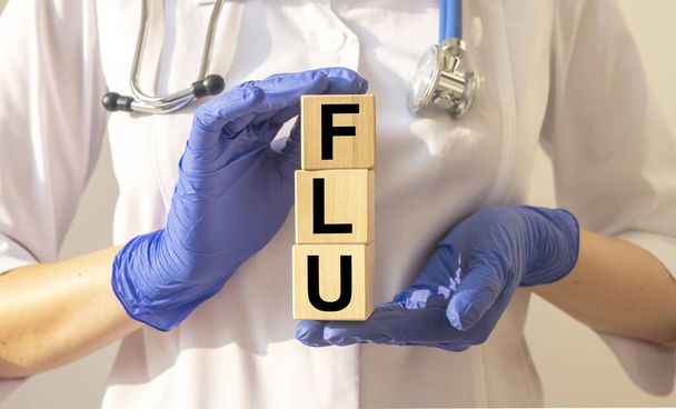 The word FLU which is made from wooden cubes. Hands in a blue glove. - Фото, зображення