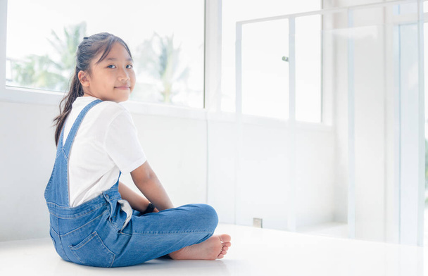 Симпатична дівчина в джинсовому комбінезоні сидить у білому будинку, розважається і розслабляється концепція
 - Фото, зображення