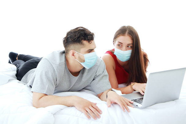 Valkoihoinen pari yllään naamio estää covid-19 virus makaa kannettavan sosiaalisen median tekniikka makuuhuoneessa. Sosiaalinen etäisyys ja terveydenhuolto Naimisissa perheen elämäntapa lomalla Käsite. - Valokuva, kuva