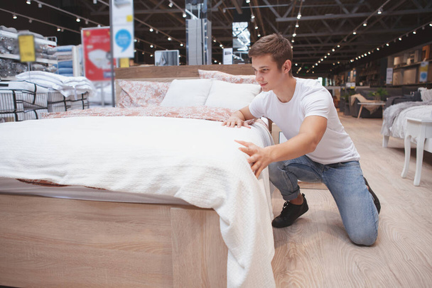 Full length shot of a handsome young man choosing new bed to buy at local furniture store - Фото, изображение
