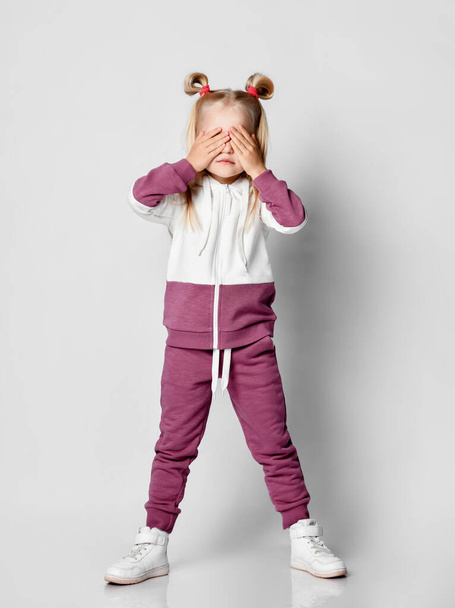 Shocked little blonde girl posing in the studio on a gray background. - Foto, afbeelding